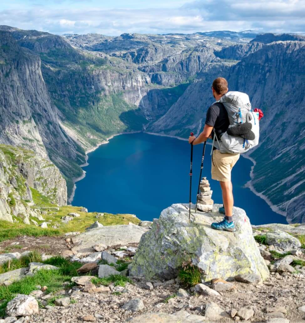 Man backpacking standing on a rock overlooking a large lake and mountains.