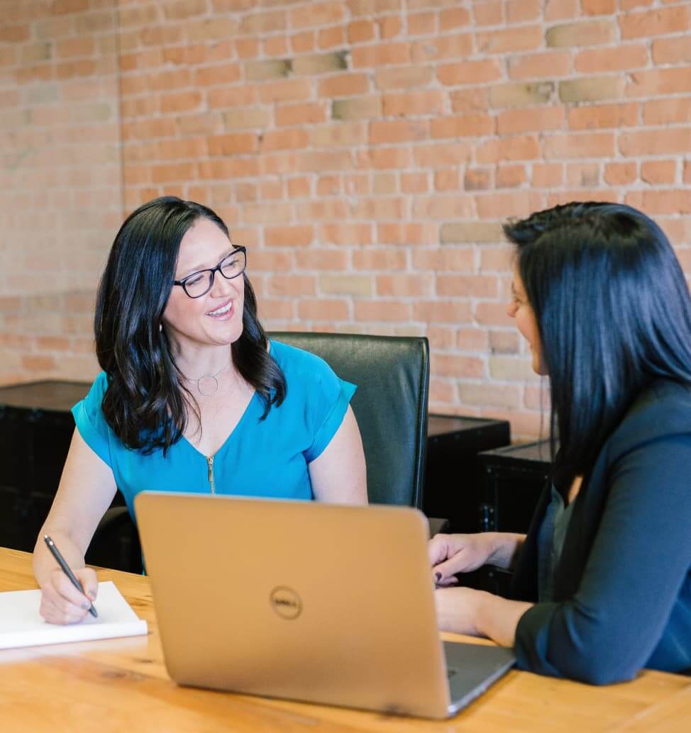 Two women meeting at a conference table with a laptop.